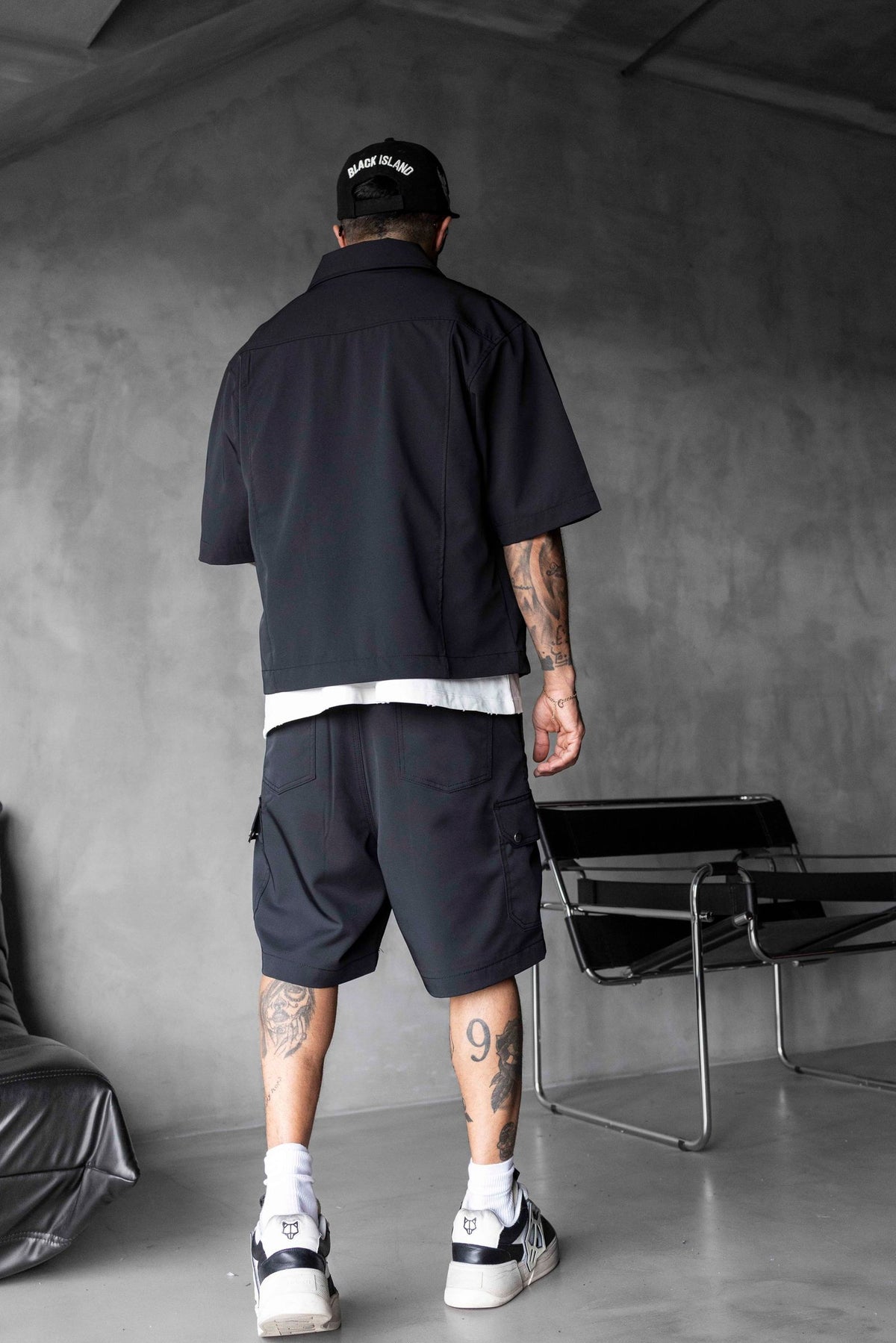 Person wearing a black shirt and shorts in a minimalistic room.