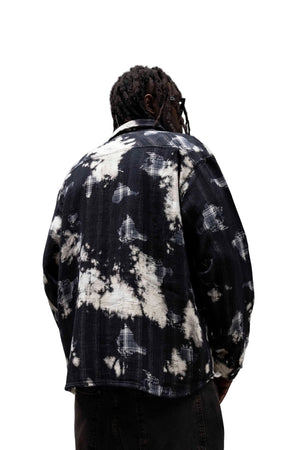 A man viewed from behind wearing a black and off-white tie-dye patterned shirt jacket in a minimalist concrete setting.