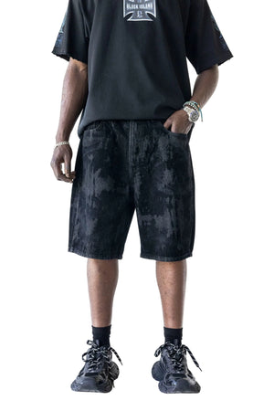 A person wearing black acid-wash shorts with a black graphic t-shirt, black socks, and black sneakers, shown from the chest down against a white background.