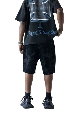A model from the back wearing a black graphic t-shirt and black distressed denim shorts, paired with black socks and black sneakers, against a plain white background.