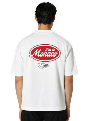 A man viewed from the back wearing a white short-sleeve t-shirt with a large red oval 'Pas de Monaco' graphic and a black signature print on the back, set against a light gray studio background.
