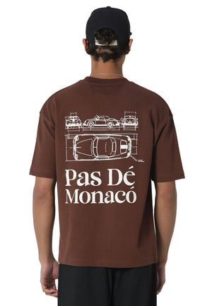 A man wearing a brown t-shirt from the back, featuring a white graphic of classic cars and the text 'Pas Dé Monaco'.
