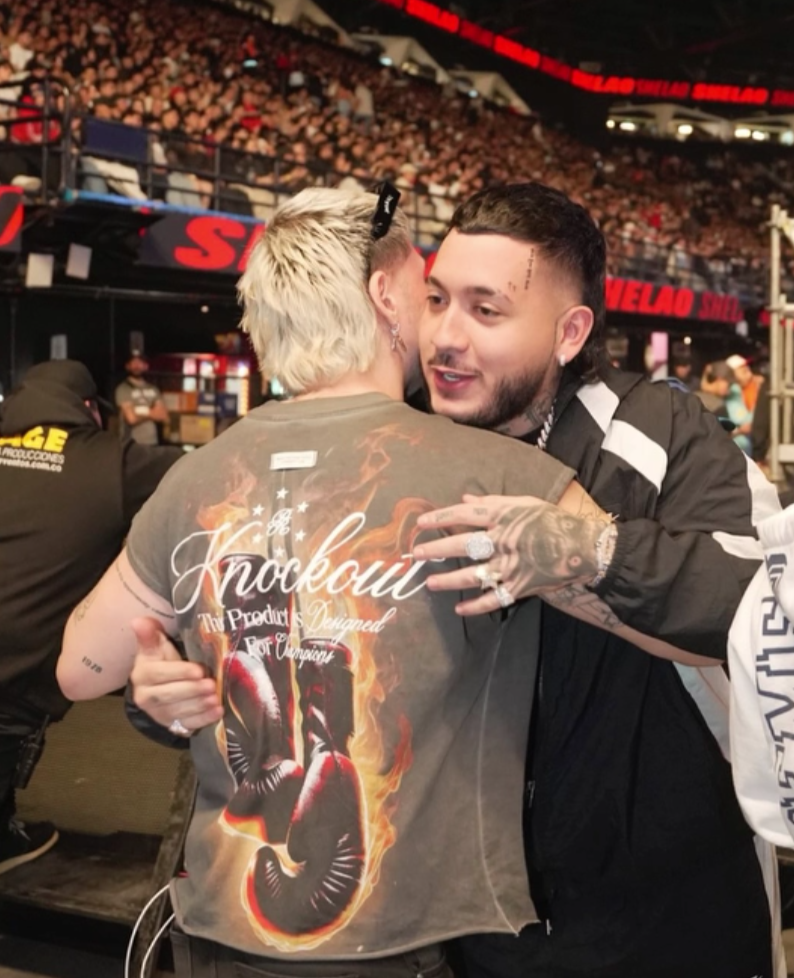 Kris R hugging in a boxing arena with a crowd in the background
