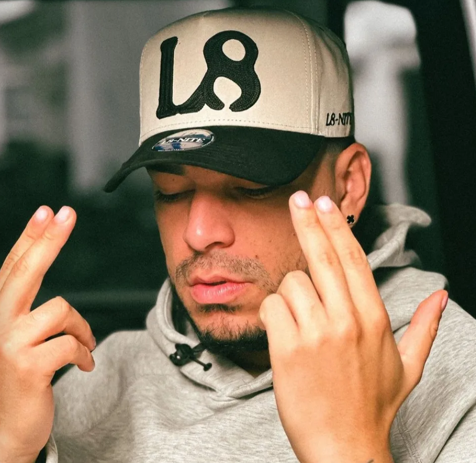 Ryan Castro wearing a cap with 'L8' logo, making a peace sign.