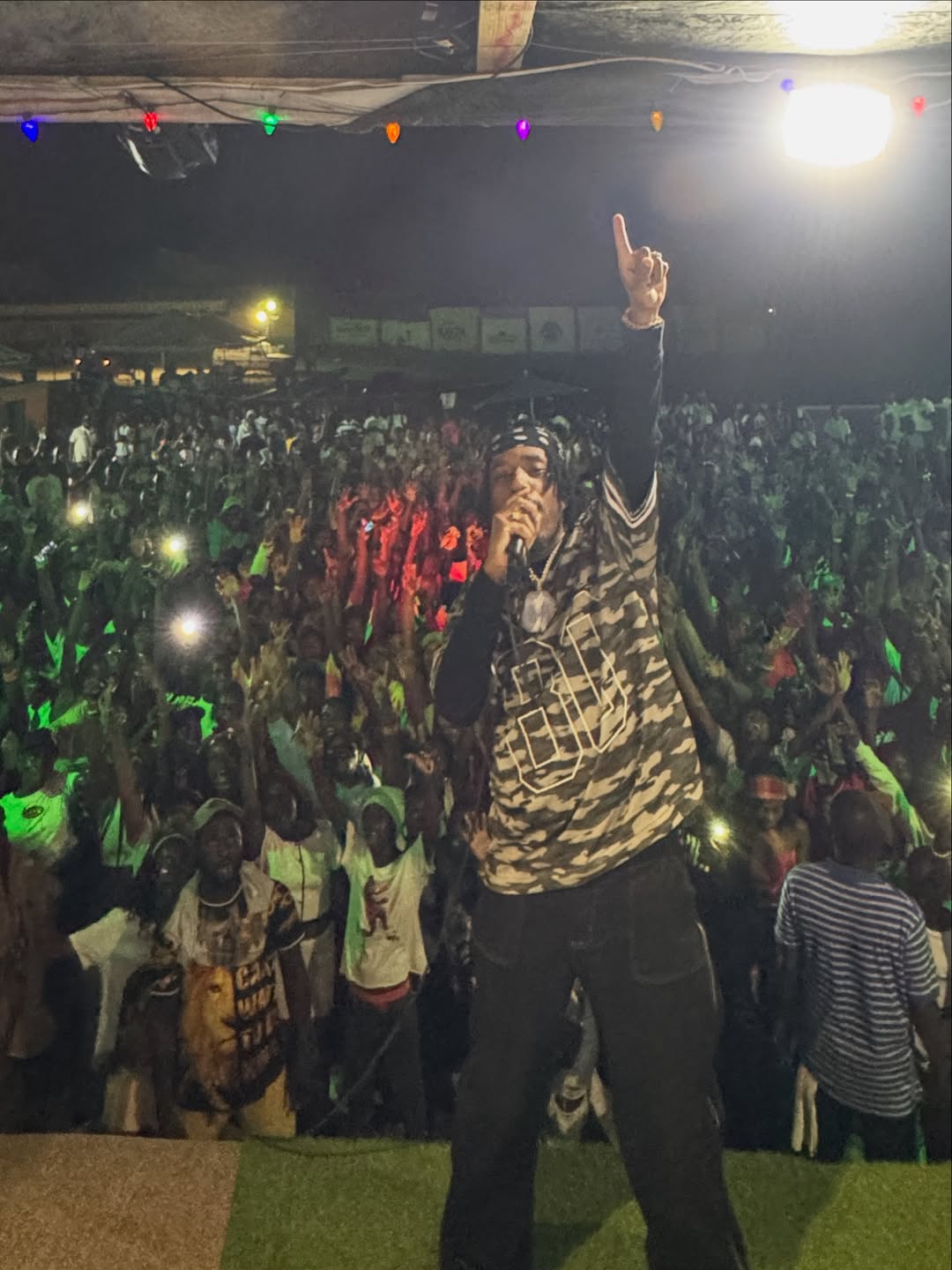 Steves J Bryan on stage with raised arm in front of a large crowd at night