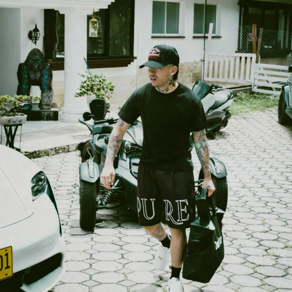 Westcol  walking with a suitcase near a sports car on a driveway wearing Pure Worldwide