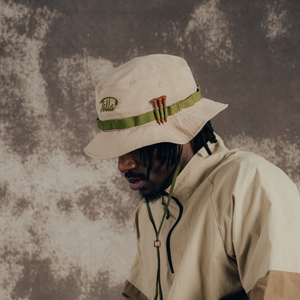 Person wearing a beige hat with a brand logo and green lanyard against a textured brown background